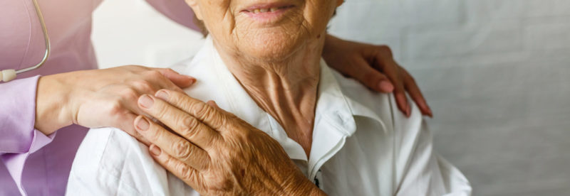 Elderly woman receiving compassionate care with a caregiver's hand on her shoulder, reflecting the nurturing environment at Burnett Medical Center's Continuing Care Center.
