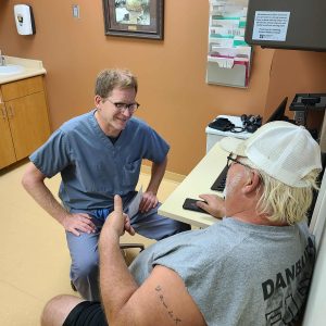 Doctor in scrubs engaging with patient in a medical office, emphasizing compassionate care and patient communication at Burnett Medical Center.