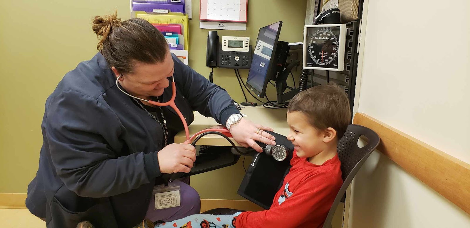 AD_4nXev1bUPO1W_eeSDQx5xUWJGTMnlgcMtFtph_T4XsAE4KWt6fHvBRPZyhVtzZLW37nbJgCg72R7fmF3hbSJLn2r8-2eJxDbxCI9gbMQR2gpAEbJIlATWvb29x5qUtWrKSWv4adgV6g Nurse using a stethoscope to check the blood pressure of a young boy in a medical office, emphasizing the importance of family healthcare and provider relationships at Burnett Medical Center.