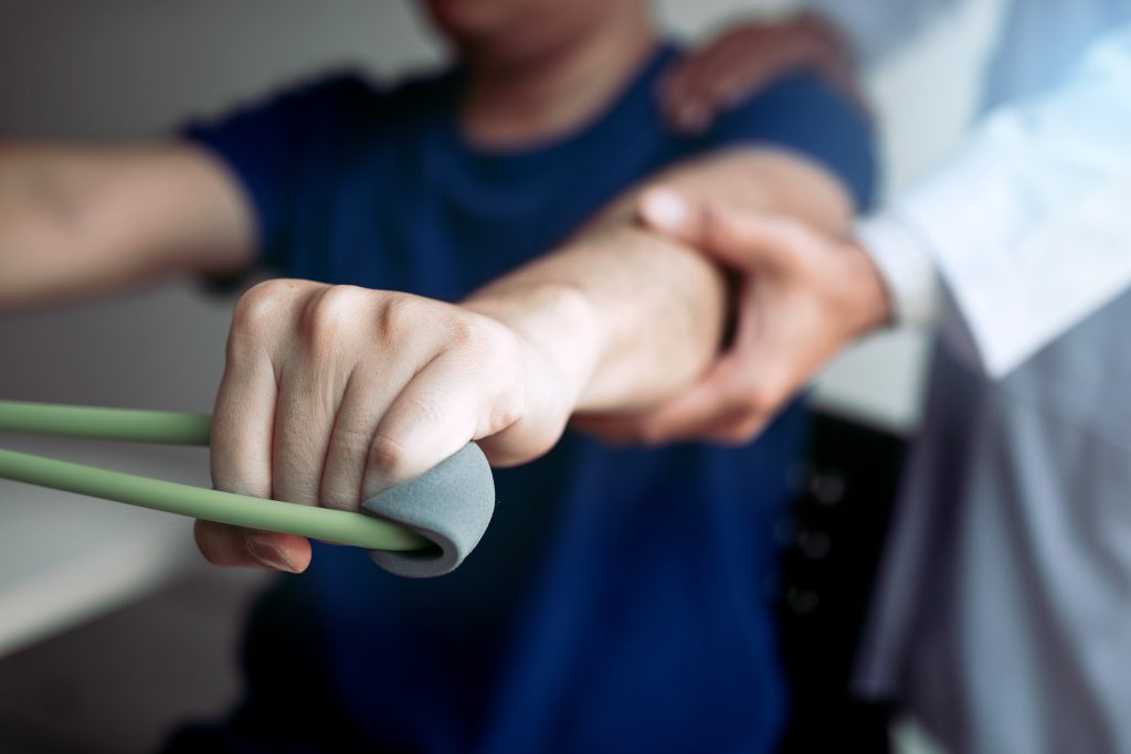 Patient performing physical therapy exercise with resistance band, assisted by a healthcare professional, focusing on rehabilitation after surgery at Burnett Medical Center.
