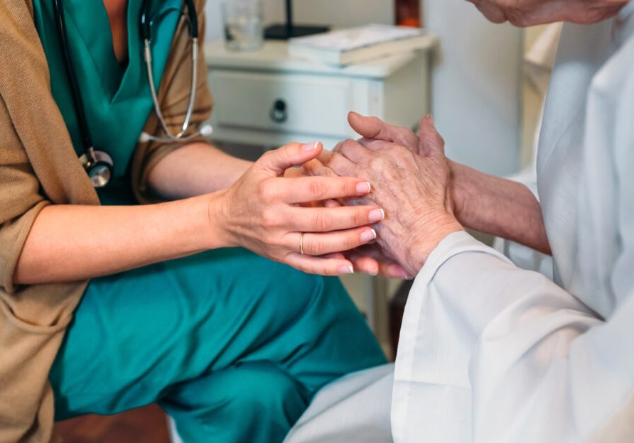 Healthcare professional holding hands with elderly patient, symbolizing compassionate care and connection at Burnett Medical Center in Grantsburg, WI.